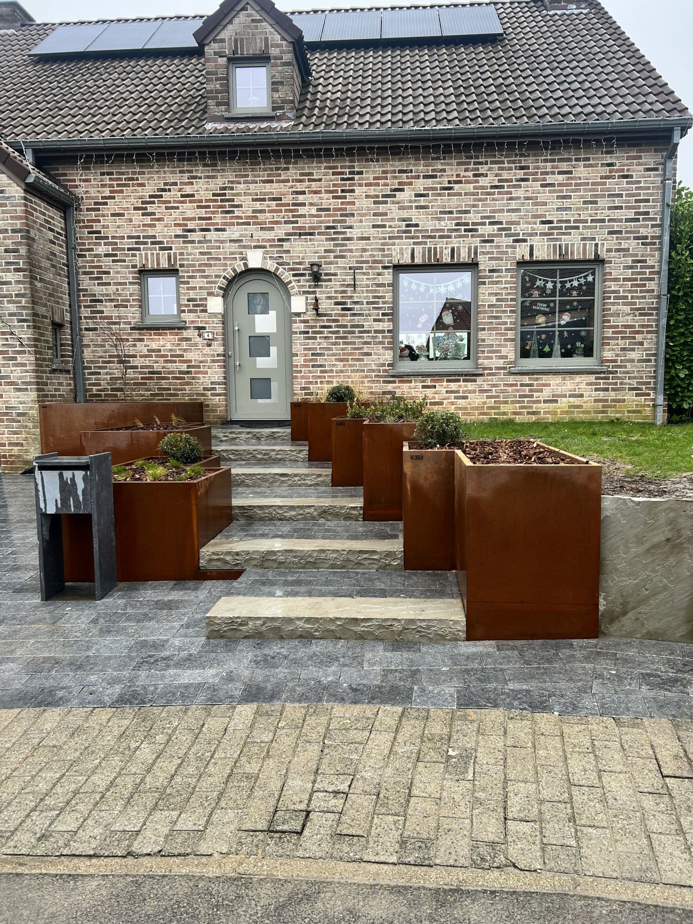 Devanture en pavés avec escalier vers la porte d'entrée, encadré de grands bacs plantés