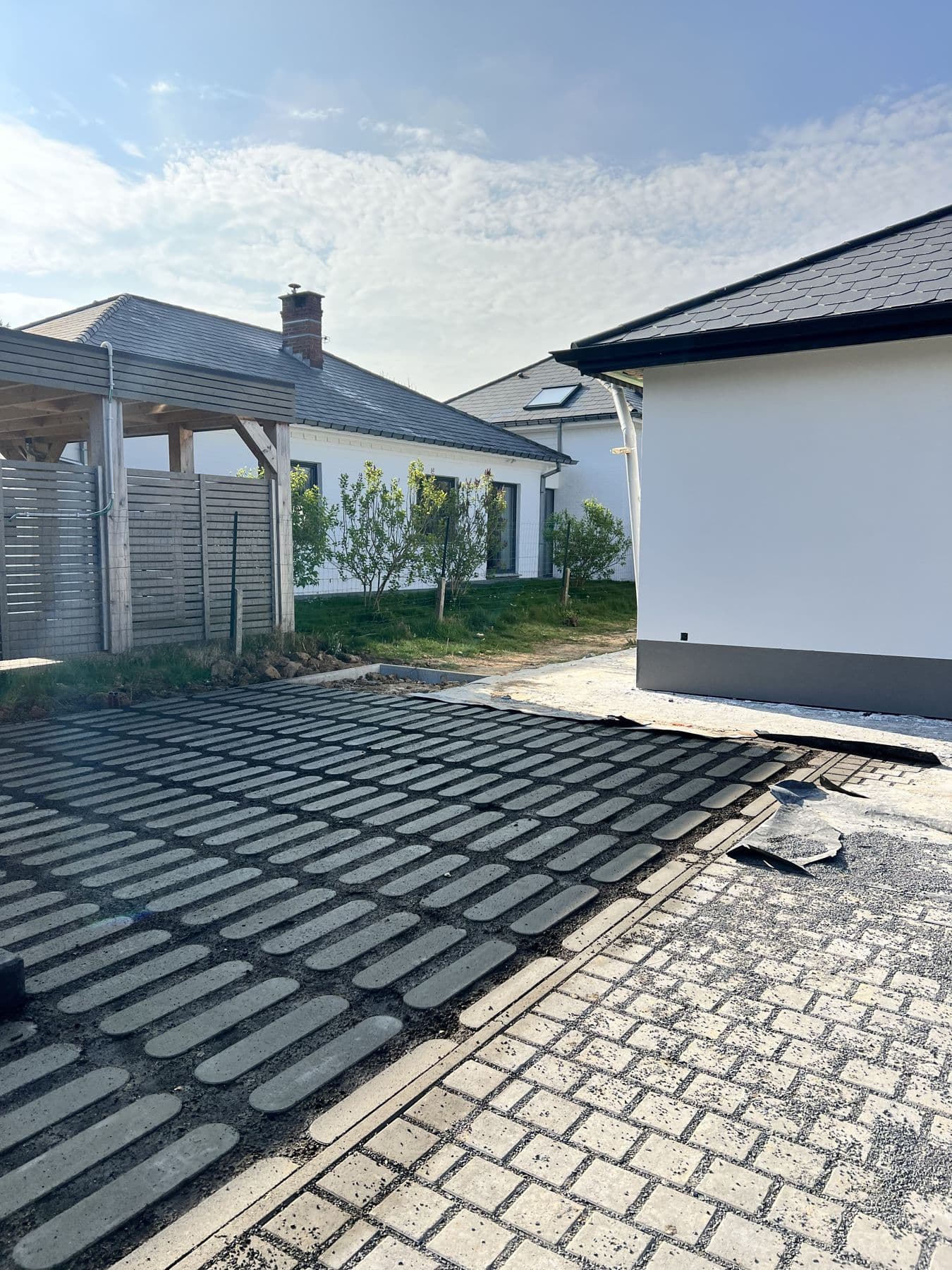 Accès carrossable en pavés avec des bandes de pavés foncés, devant une maison blanche et un carport