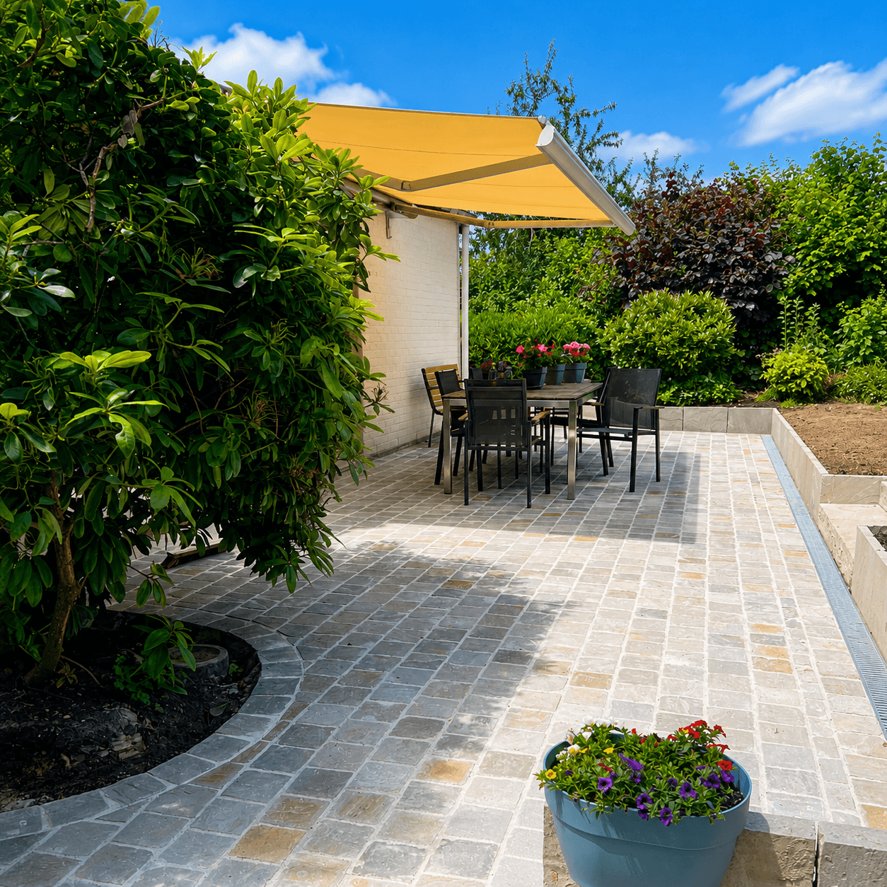 Terrasse en pavés clairs avec mobilier, sous une toile jaune, bordée d'un muret