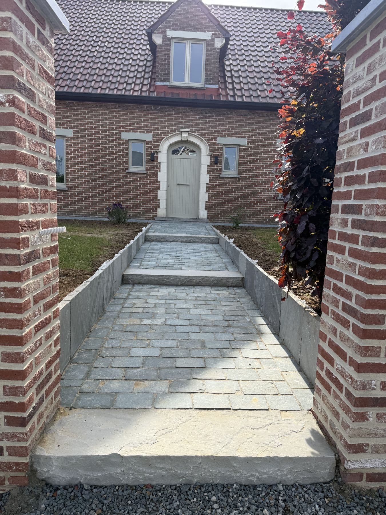 Allée d'entrée en dalles de pierre entre deux murets, menant à la porte d'une maison en briques